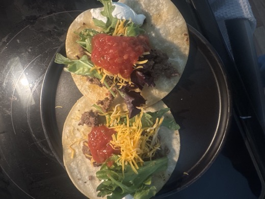 Two tacos with beef, cheese, greens, salsa, and sour cream